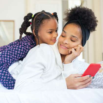 Mom and daughter lie in bed and check a mobile phone together