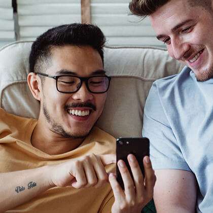 Two casually dressed young guys smile at something on a mobile phone