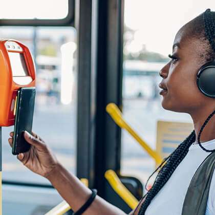 Young woman in braids and headphones uses her mobile phone to access public transportation