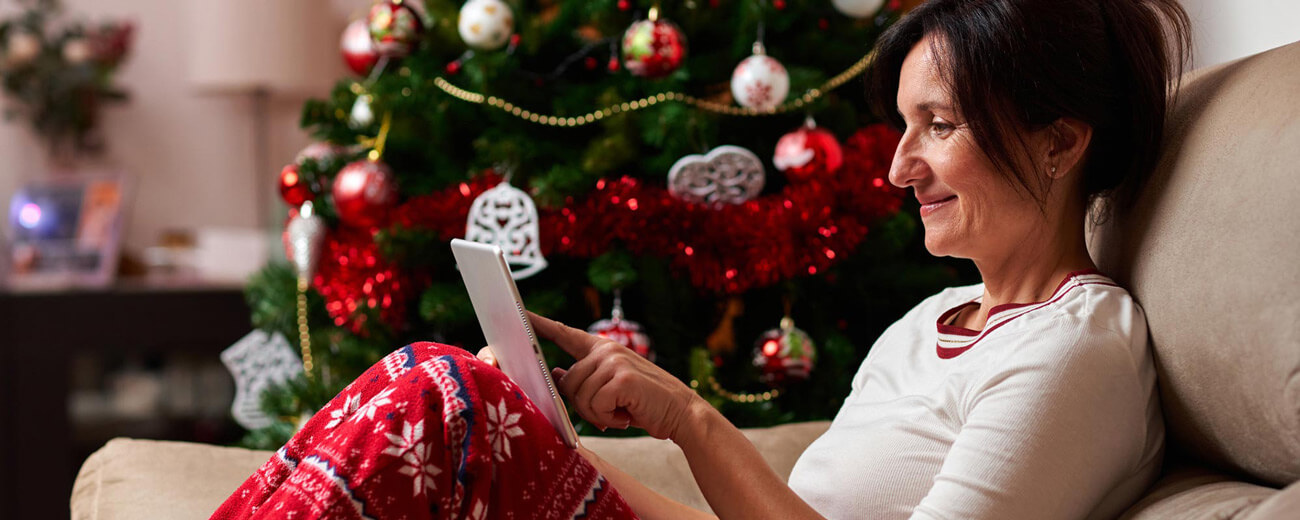 woman sitting on a couch looking at her tablet during the holiday season
