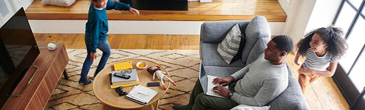 father sitting on the couch working on his computer while his kids run around the livingroom