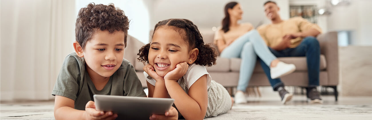 Two kids on a tablet with mom and dad in the background