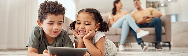 Two kids on a tablet with mom and dad in the background