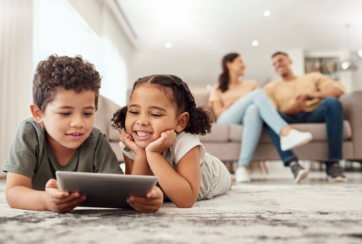 Two kids on a tablet with mom and dad in the background