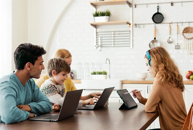 Family working around the kitchen table on multiple devices