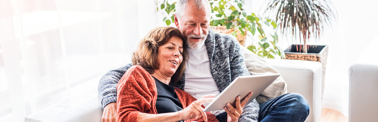 Retired couple reviews cybersecurity resources on a tablet from the comfort of their sofa