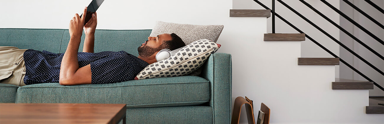 man lying on sofa with tablet and headphones researches internet options