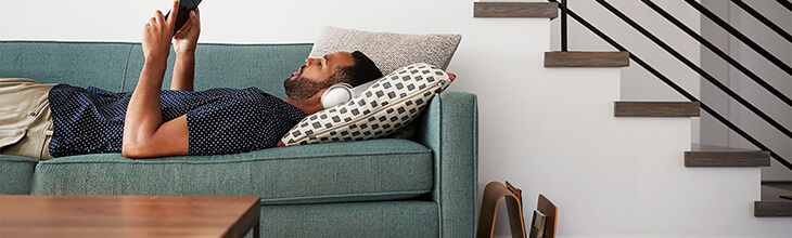 man lying on sofa with tablet and headphones researches internet options