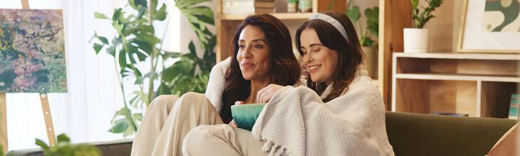 Mother & daughter watching shows together wrapped in a blanket