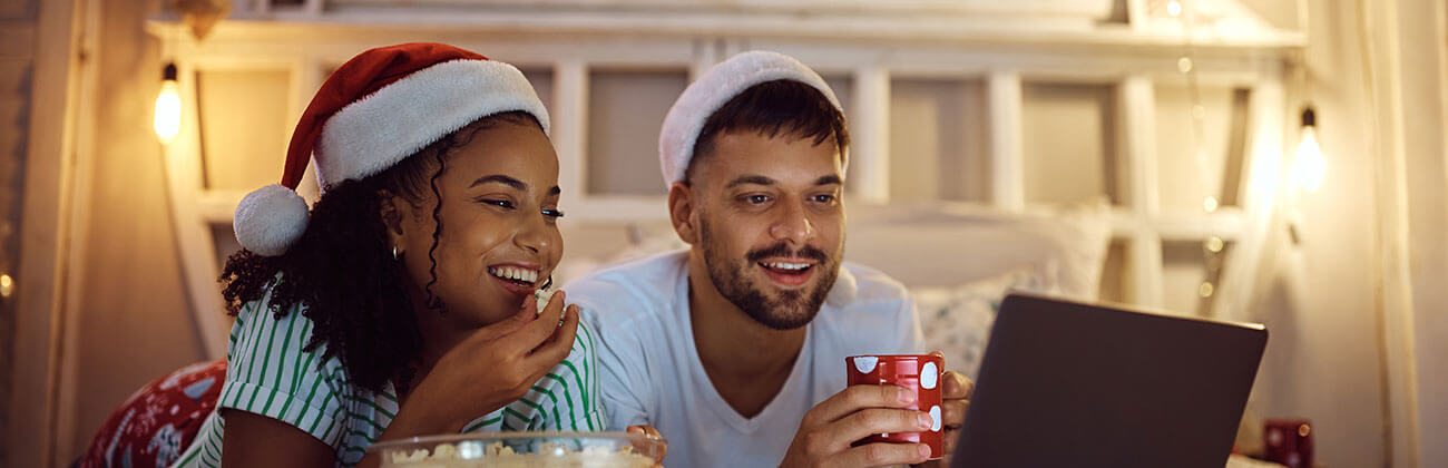 Young couple enjoys streaming movies with popcorn, holiday decorations, and Santa hats