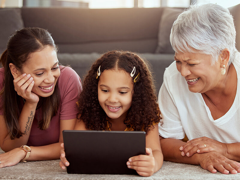 3 generations of woman watching a tablet while laying on the floor